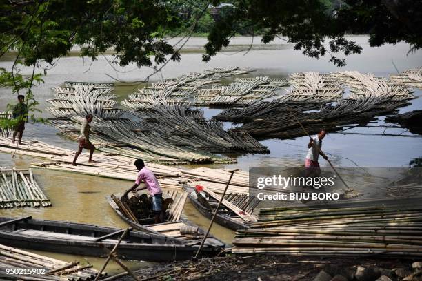 Indian labourers push heaps of bamboo along Howrah river to be used in the construction industry and sold at a floating market, in Chakmaghat...