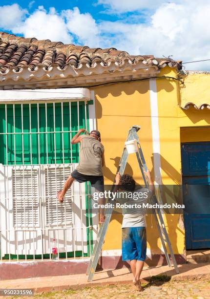 Two middle age men painting outside of a vintage colonial house. Trinidad's colorful houses are its biggest tourist attraction requiring a lot of...