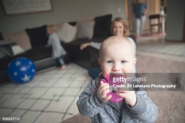 12 month old baby chews on toy while mothers looks behind him - gezahnt stock-fotos und bilder