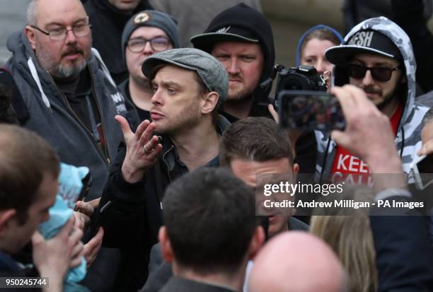 People gesture as former English Defence League leader Tommy Robinson speaks to the media outside Airdrie Sheriff Court after Mark Meechan was fined...