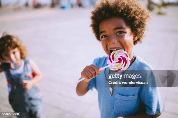 multi-ethnic brothers eating colourful lollipops outdoors in summer - lollipop boys stock pictures, royalty-free photos & images