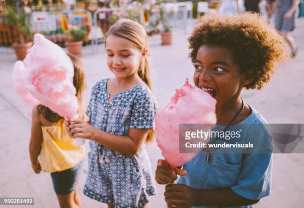 y multiétnicos niños comiendo algodón de azúcar en el parque de atracciones - algodón de azúcar fotografías e imágenes de stock