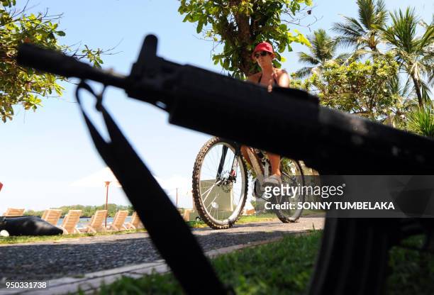 In this photograph taken on November 13, 2011 a tourist rides a bicycle where armed Indonesian marine policemen posted at the beach area in Nusa Dua...