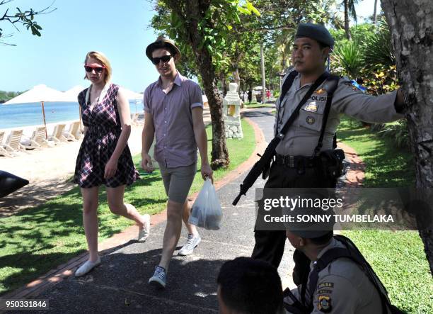 In this photograph taken on November 13, 2011 tourists walk pass armed Indonesian marine policemen posted at the beach area in Nusa Dua near the...