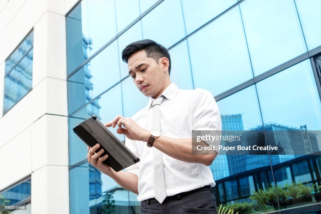 Man looking down at his tablet computer and looking around for locations, while standing in front of the business district
