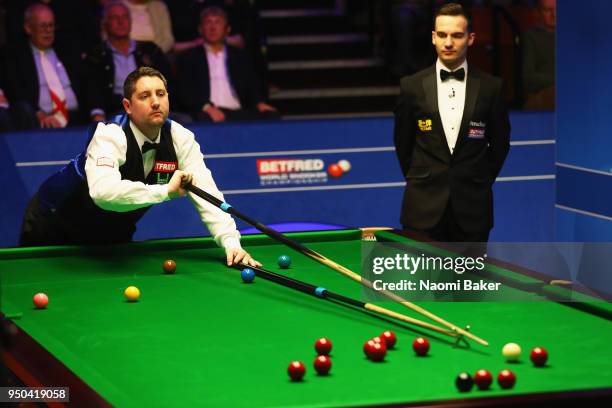 Stuart Carrington of England plays a shot during his first round match against Barry Hawkins of England as match Referee Marcel Eckardt looks on...