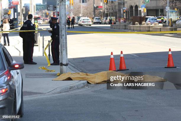 Police officers stand near a body that is covered up after it was hit after a truck drove up on the curb and hit several pedestrians in Toronto,...