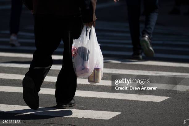 Pedestrian carries a plastic shopping bag across Atlantic Avenue, April 23, 2018 in the Brooklyn borough of New York City. New York Governor Andrew...