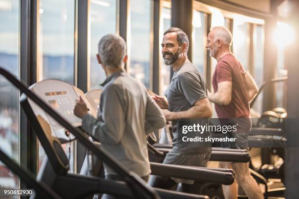 drie actieve senioren uitoefenen op loopbanden in een healthclub en communiceren. - 3 old men jogging stockfoto's en -beelden