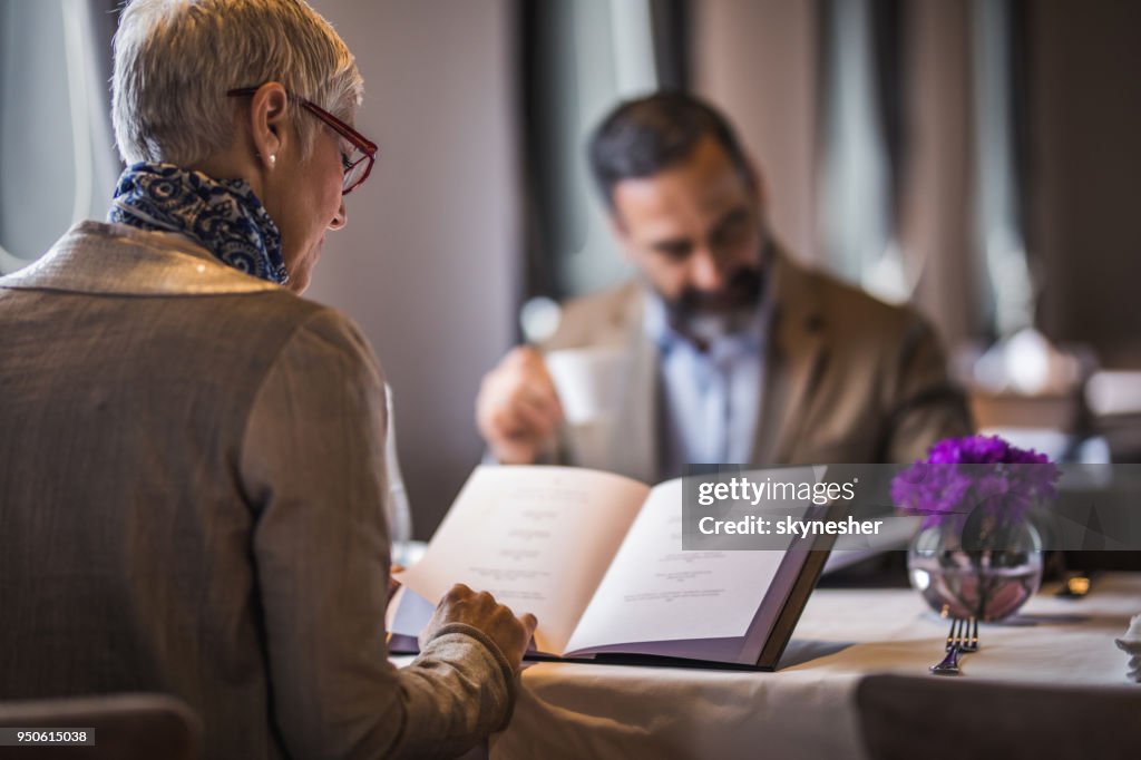 Back view of mature woman reading Menu during lunch time in a restaurant.