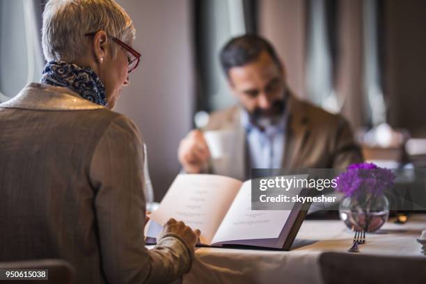 back view of mature woman reading menu during lunch time in a restaurant. - menu stock pictures, royalty-free photos & images