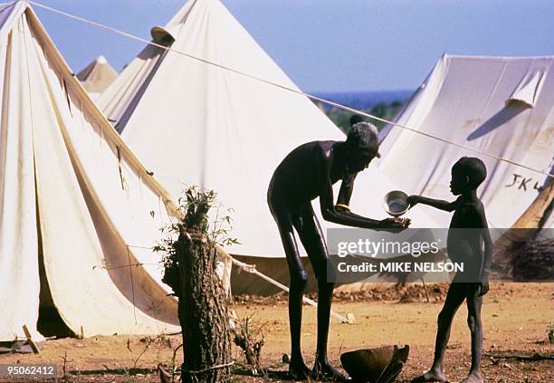 Boy, belonging to Mundari displaced ethnic group, gives some water in September 1986 to an old starving man in a UNHCR refugee camp outside Juba, the...