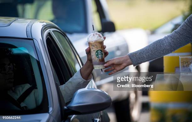 An employee passes a drink order to a customer at the drive-thru of a Starbucks Corp. Coffee shop in Rodeo, California, U.S., on Monday, April 23,...