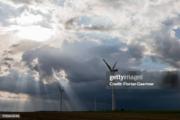 Wind turbines are pictured in front of dark clouds and the shining sun on April 13, 2018 in Melaune, Germany.