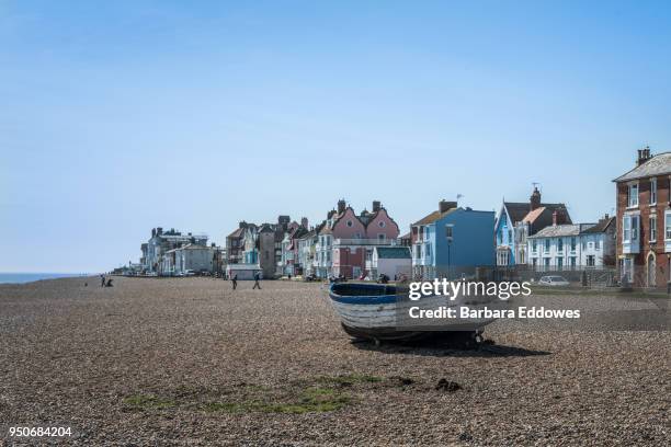 a small boat on a beach with houses in the background in aldeburgh, suffolk - aldeburgh stock pictures, royalty-free photos & images