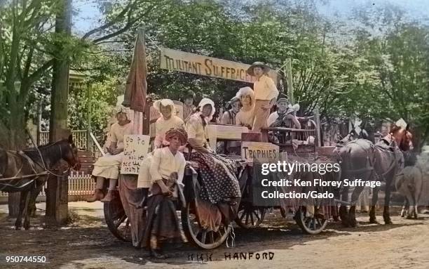 Black and white photograph showing men and boys, some dressed in women's Edwardian clothing, seated and standing on a horse-drawn, anti-suffrage...