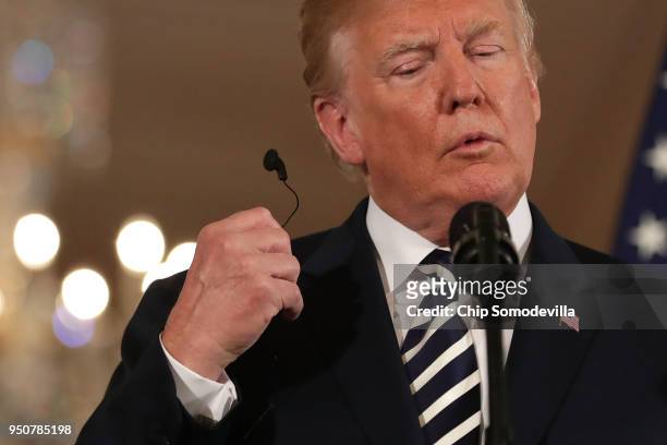 President Donald Trump pulls out an audio ear bud for translation during a joint news conference with French President Emmanuel Macron in the East...