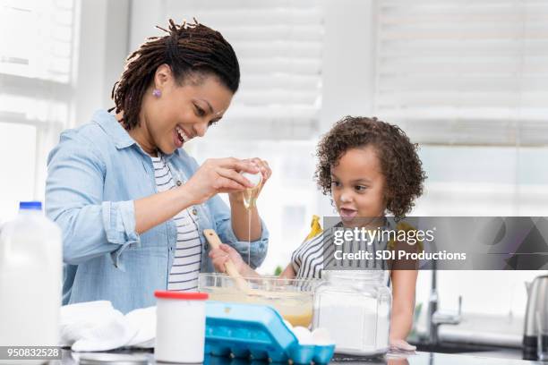 happy mom teaches young daughter to bake - crack spoon stock pictures, royalty-free photos & images