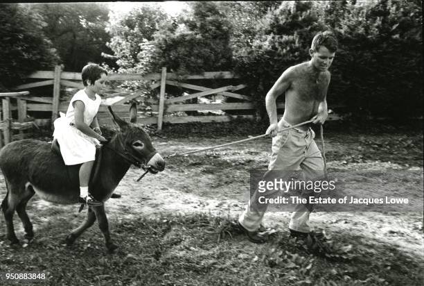 View of shirtless US Attorney General Robert F Kennedy as he pulls his daughter, Kathleen , on a donkey on the grounds of their home, Hickory Hill,...