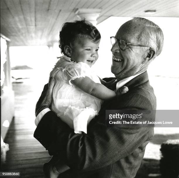 View of American businessman Joseph P Kennedy Sr as he holds his granddaughter, Caroline, on the porch of his home, Hyannis Port, Massachusetts, late...