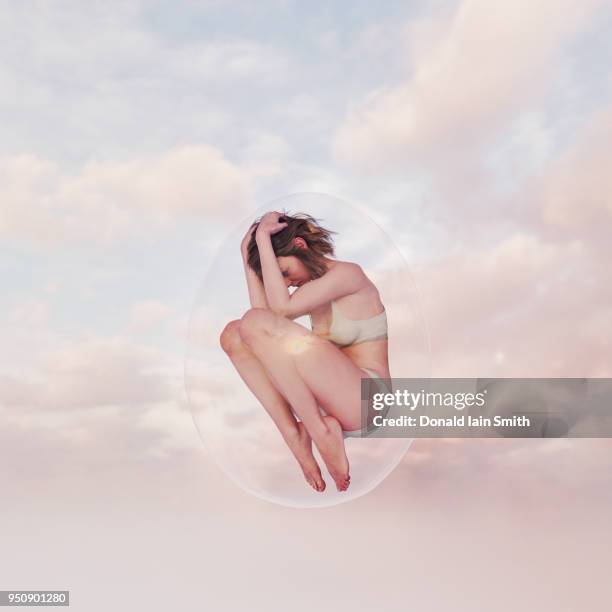 young woman curled up inside transparent glass egg floating in sky - woman curled up stock pictures, royalty-free photos & images