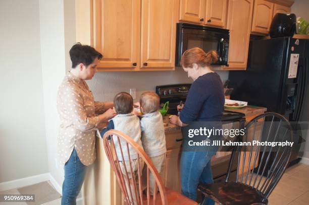 lesbian mothers help teach twin toddlers cooking at home - fraternal twin stock pictures, royalty-free photos & images