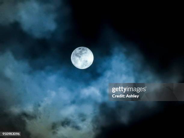 close up detail of a full moon shining through bluish clouds - vollmond stock-fotos und bilder