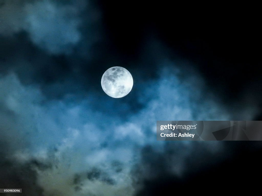 Close up detail of a full moon shining through bluish clouds