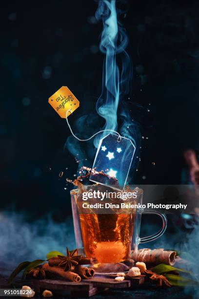 teabag with shining stars above a double wall tea cup with a steam and a dynamic splash. astronomy teatime concept on a dark background with copy space. - liquid galaxy stock pictures, royalty-free photos & images