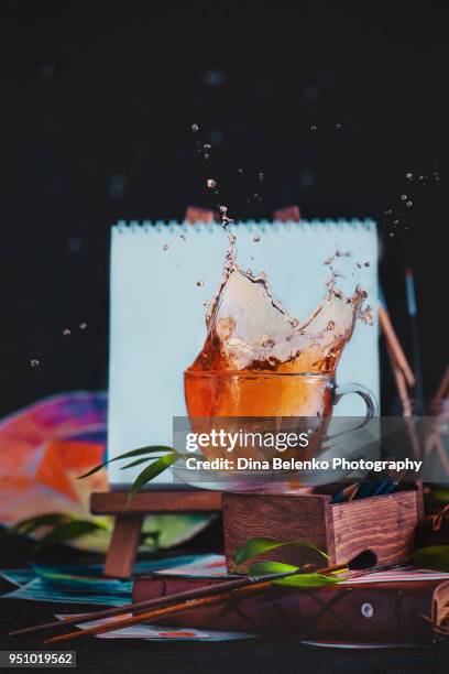 splash in a tea cup in front of an artist easel with blank canvas. painting tea time concept with action food photography. - action painting stock-fotos und bilder