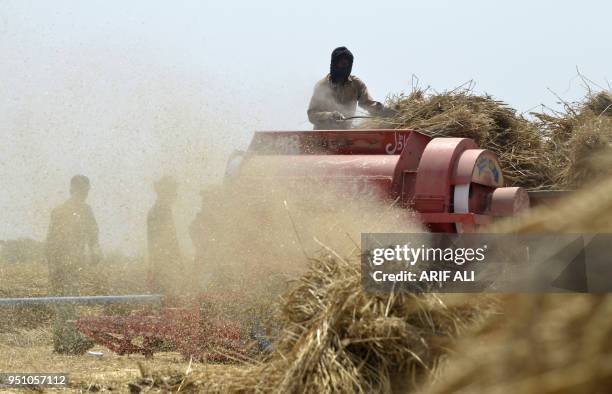 Pakistani farmers use a threshing machine to refine wheat during harvesting in a field on the outskirts of Lahore on April 25, 2018.