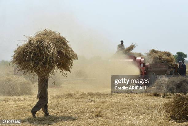 Pakistani farmers use a threshing machine to refine wheat during harvesting in a field on the outskirts of Lahore on April 25, 2018.