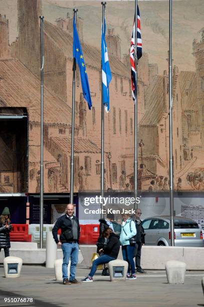 The Scottish saltire, the Union flag, and the flag of the European Union fly outside the Scottish Parliament, against a backdrop of a mural screening...