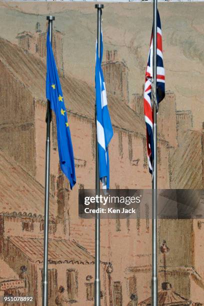 The Scottish saltire, the Union flag, and the flag of the European Union fly outside the Scottish Parliament, against a backdrop of a mural screening...