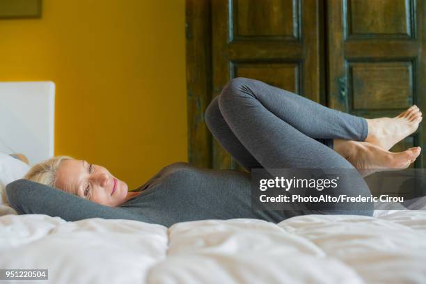 mature woman lying on bed with knees to chest - older woman legs fotografías e imágenes de stock