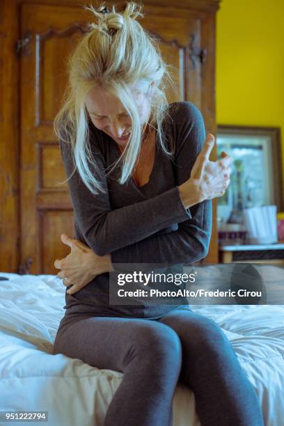 mature woman sitting on bed with arms crossed and head down, looking upset - apendicitis fotografías e imágenes de stock