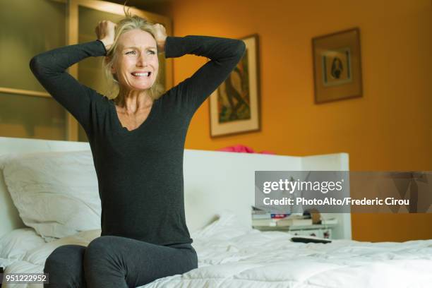 mature woman sitting on bed with hands on head in exasperation - impatient stock pictures, royalty-free photos & images