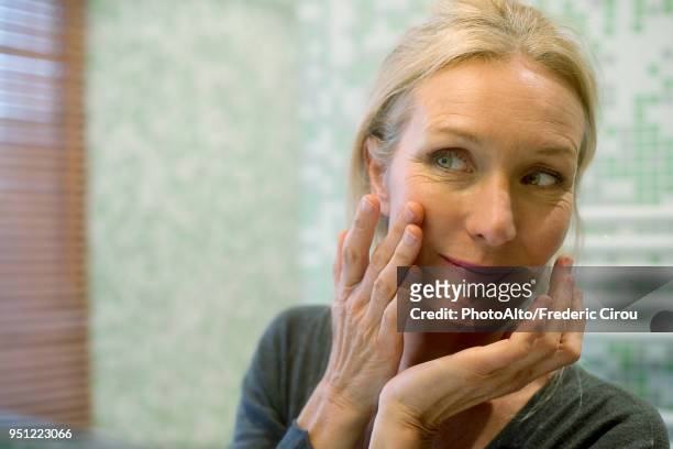 mature woman looking at reflection in mirror with hand on cheek - geriatrik bildbanksfoton och bilder