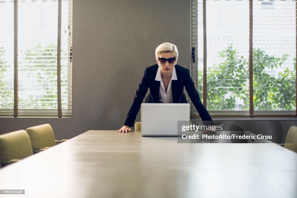 Woman in suit leaning against table looking at camera