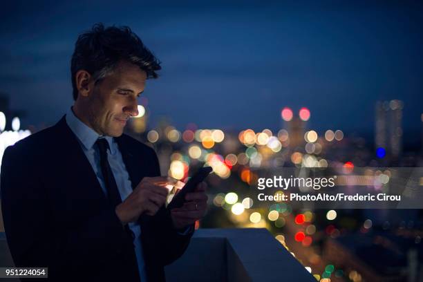 businessman on high rise rooftop using mobile phone - high rise night stockfoto's en -beelden