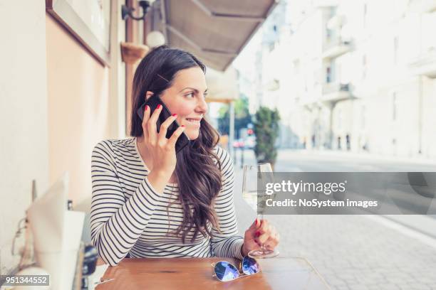 young woman drinking white wine at restaurant, using mobile phone - no drinking stock pictures, royalty-free photos & images