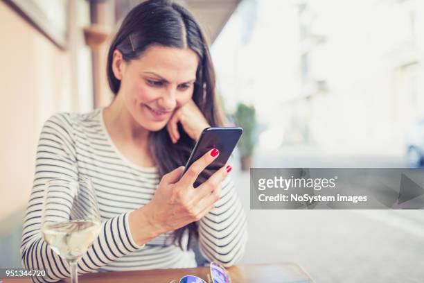 young woman drinking white wine at restaurant, using mobile phone - no drinking stock pictures, royalty-free photos & images