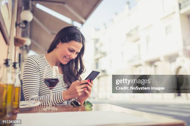 young woman drinking red wine at restaurant, using smart phone - no drinking stock pictures, royalty-free photos & images