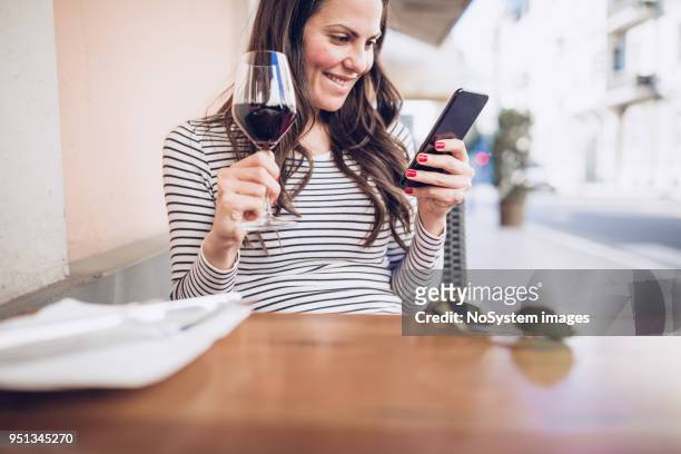 young woman drinking red wine at restaurant, using smart phone - no drinking stock pictures, royalty-free photos & images