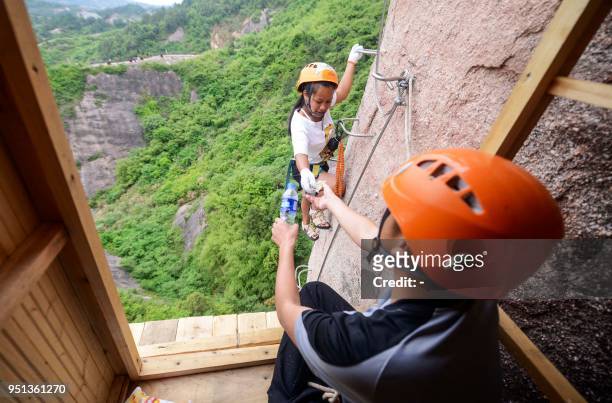 This photo taken on April 25, 2018 shows a rock climber buying a bottle of water from a 100-meter-high convenience store on a cliff in Pingjiang in...