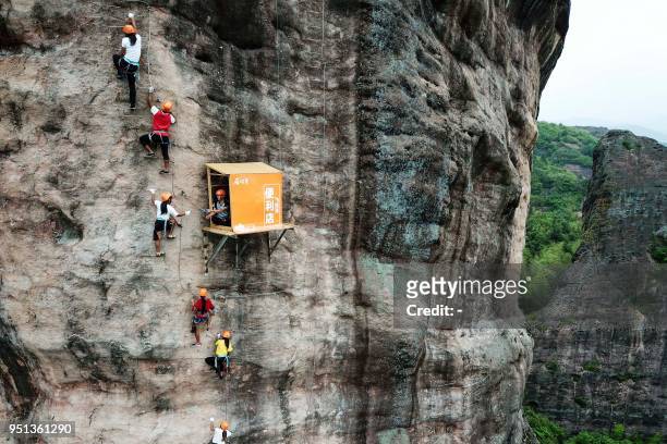 This photo taken on April 25, 2018 shows people rock climbing past a 100-meter-high convenience store on a cliff in Pingjiang in China's central...