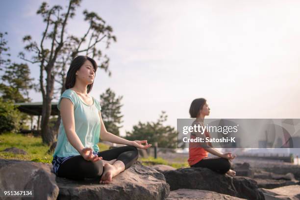 two women practicing yoga on rock - odaiba seaside park stock pictures, royalty-free photos & images