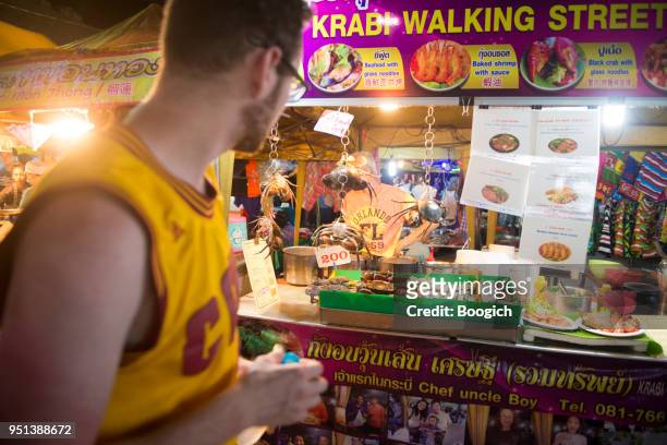 tourist walks by night market vendor krabi town thailand - krabi stock pictures, royalty-free photos & images