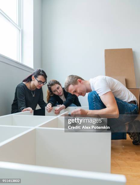 the family moving in to the new apartment. the young 30 years old man and two teenage girls, sisters, unboxing and assembling furniture. - 18 19 years stock pictures, royalty-free photos & images