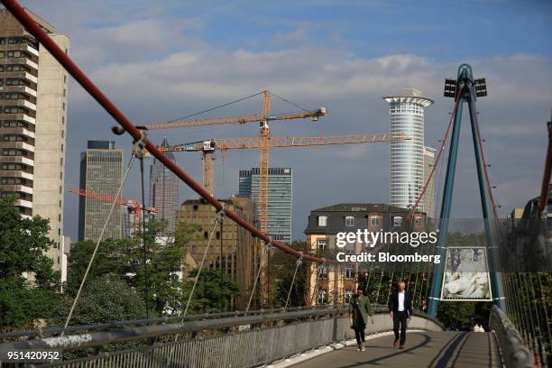 Pedestrians pass over a bridge spanning the River Main as skyscrapers and construction cranes stand beyond in Frankfurt, Germany, on Wednesday, April...